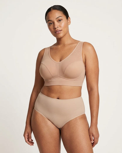 A woman modeling a beige Mesh Front Leisure Bra, photographed against a clean light gray studio background.