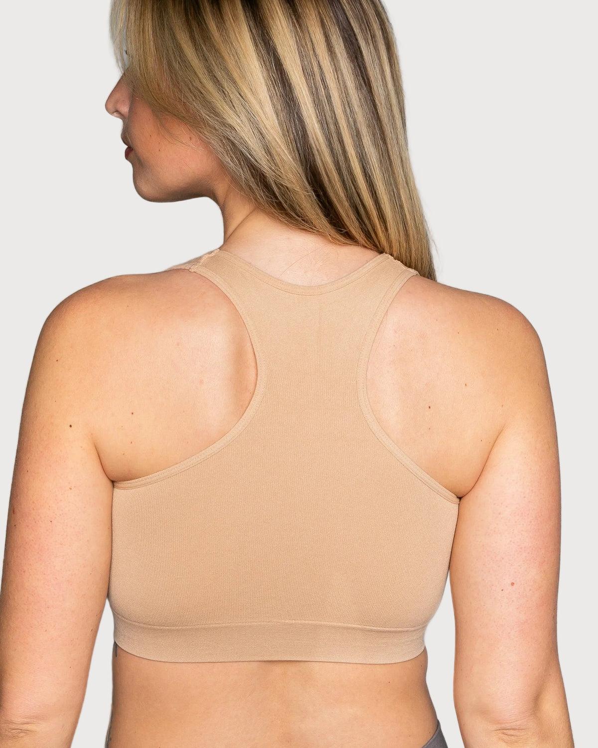 Rear view of a woman wearing a beige Seamless Racerback Ahh Bra against a light gray studio background.