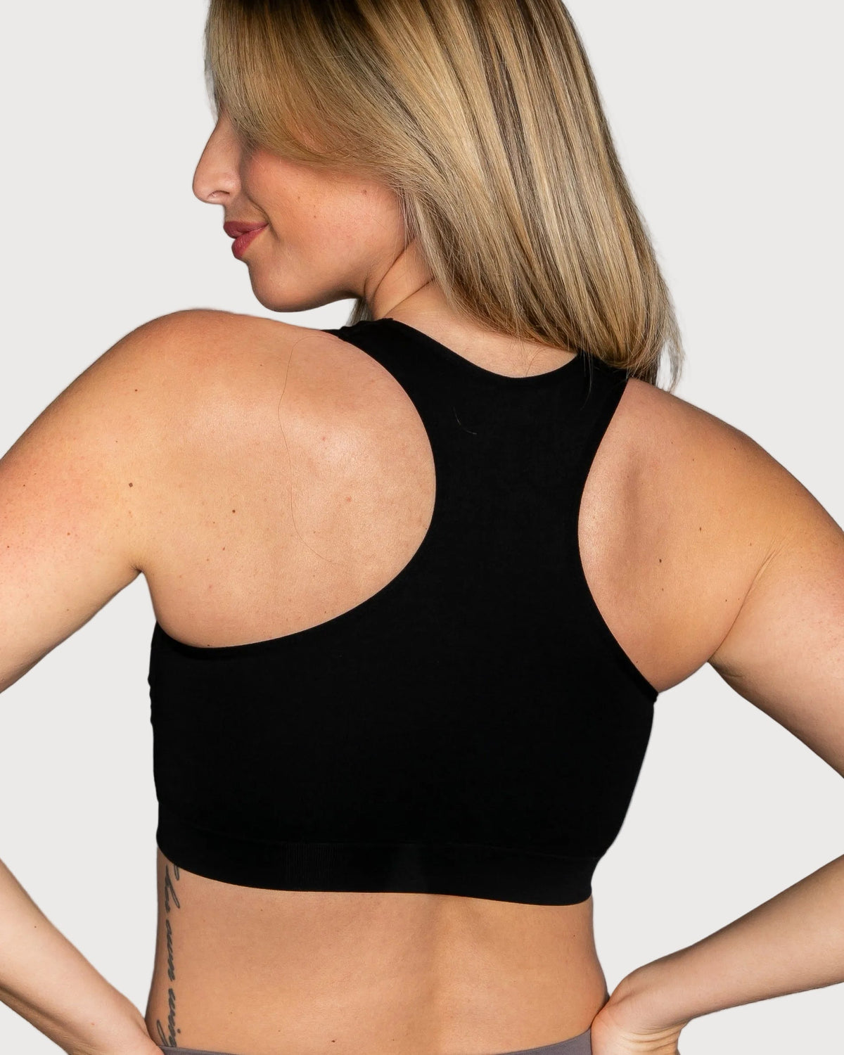 A woman shown from the back wearing a black Seamless Racerback Ahh Bra against a plain gray studio background.