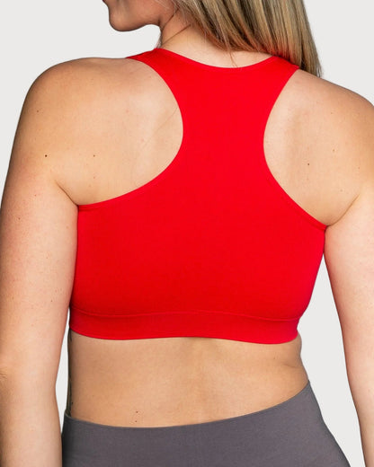 A close-up back view of a woman wearing a cherry Seamless Racerback Ahh Bra, paired with gray leggings, against a light gray studio background.