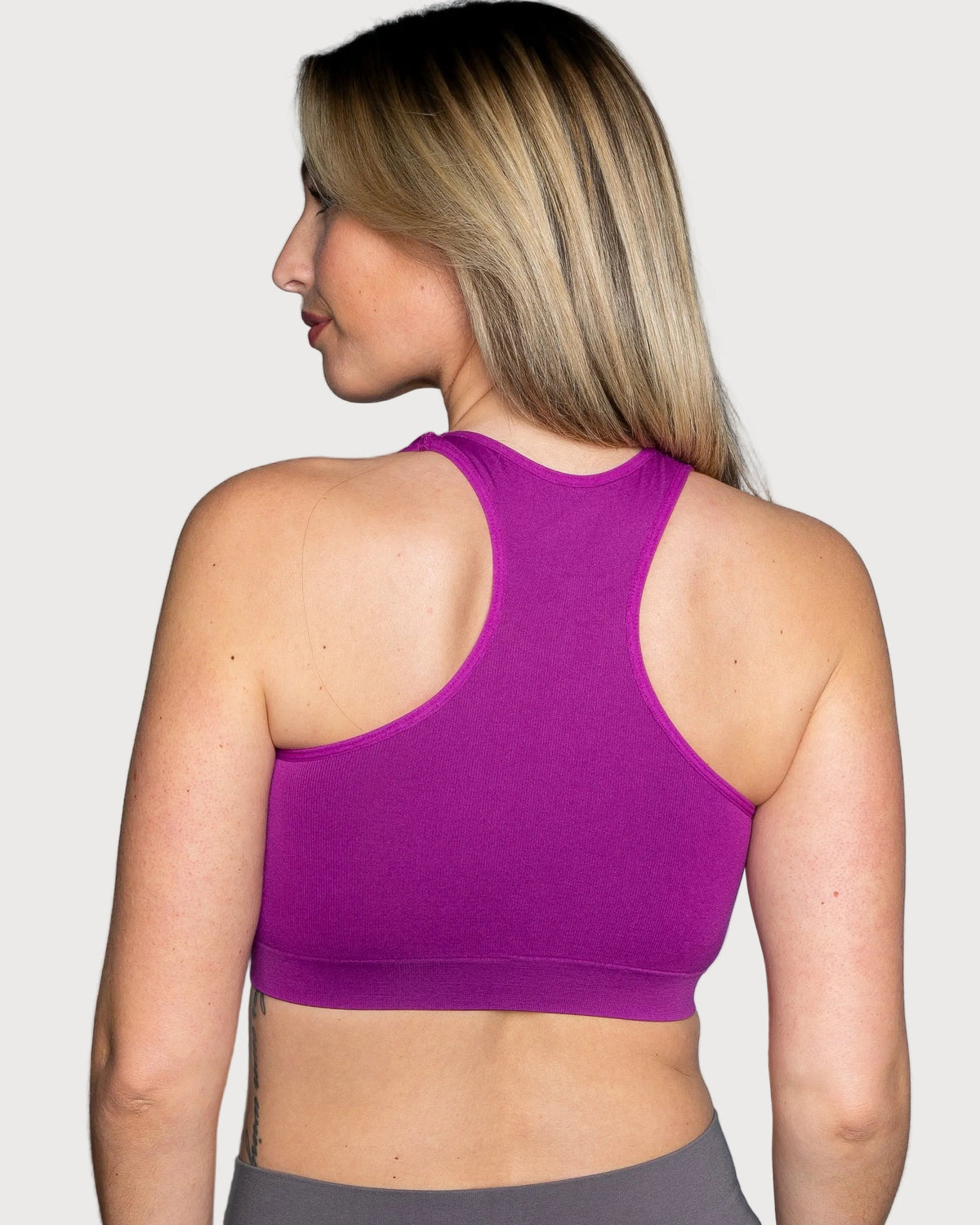 A woman shown from the back wearing a bright purple Seamless Racerback Ahh Bra, photographed against a light gray studio background.