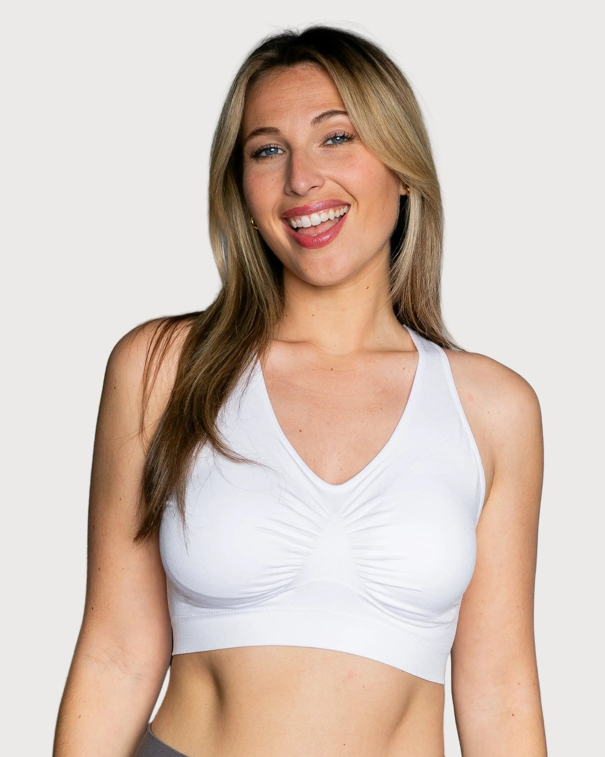 A smiling woman wearing a white Seamless Racerback Ahh Bra, photographed against a solid light gray background.